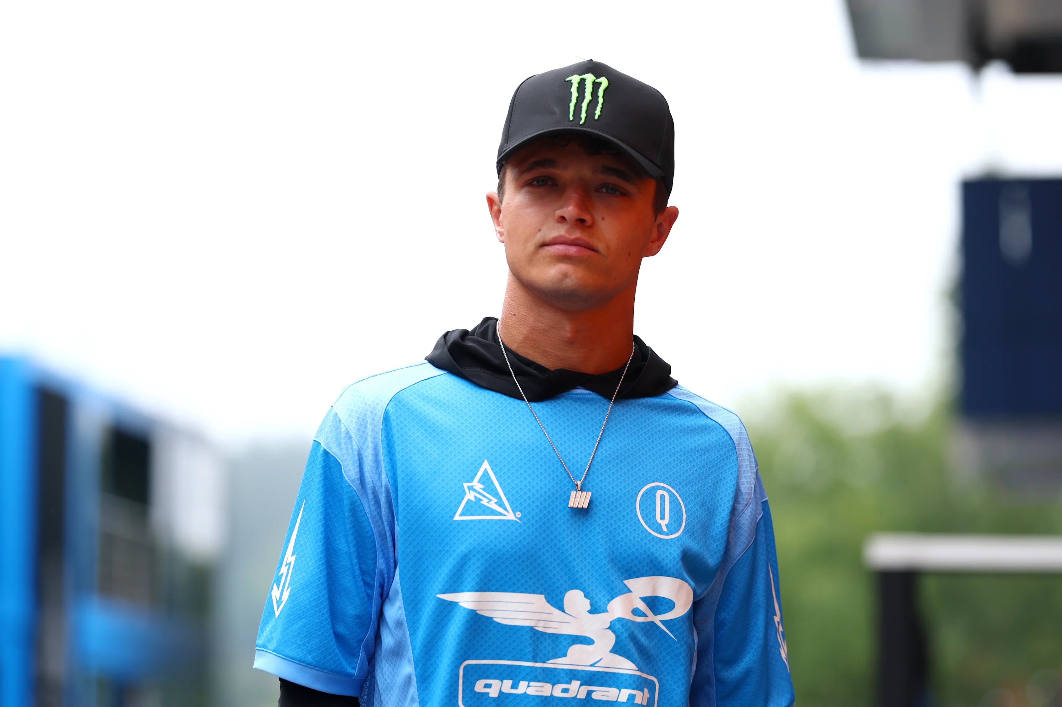 Lando berjalan paddock menjelang 2025 Grand Prix Belgium memakai baju gaya jersi dari kuadran jenamanya sendiri. Leret untuk melihat lebih banyak